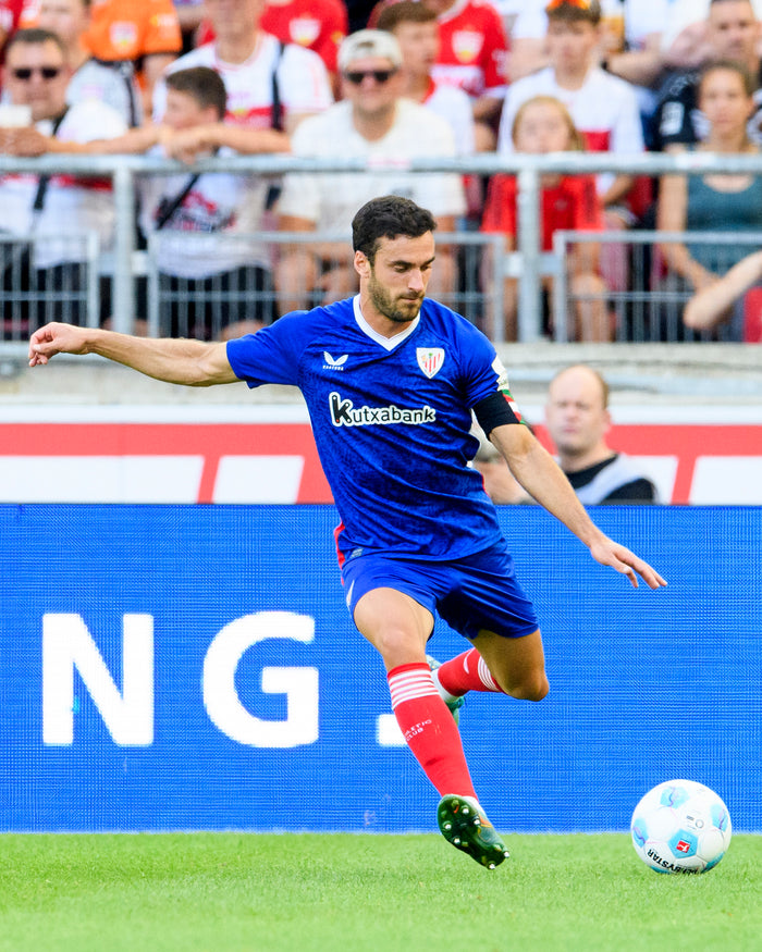 Soccer player wearing a blue away shirt on the field during a match with a crowd in the stands and Kutxabank logo visible
