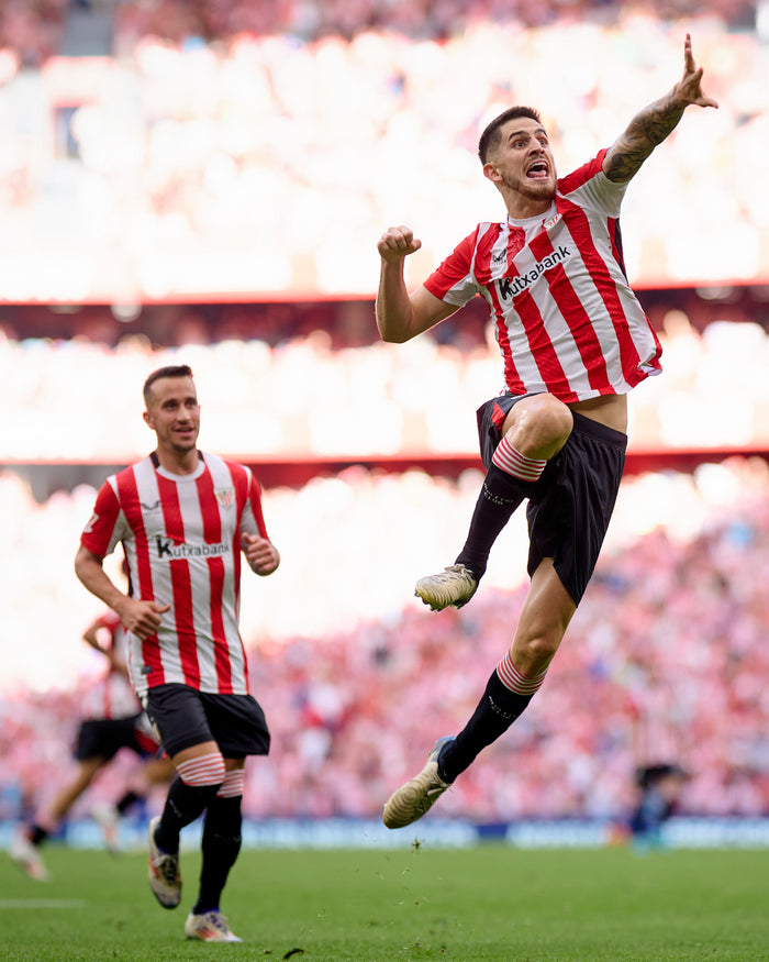 Soccer players in red and white striped Junior 24/25 home shirts celebrating on the field