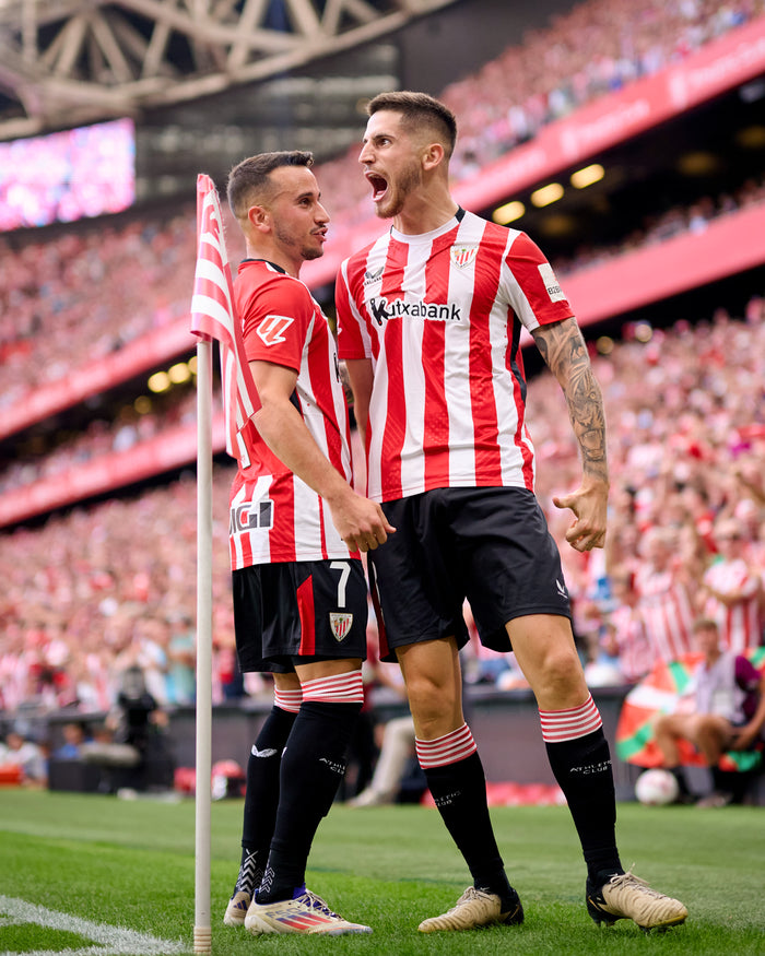 Two Athletic Club players in red and white striped home shirts celebrate on the field