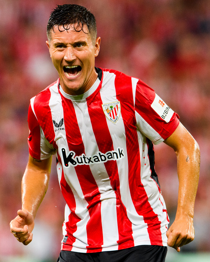 Footballer wearing red and white striped home shirt in action with Kutxabank sponsor visible
