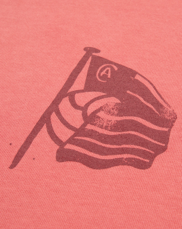 Close-up of coral fabric showing a dark flag and waves graphic on the left chest