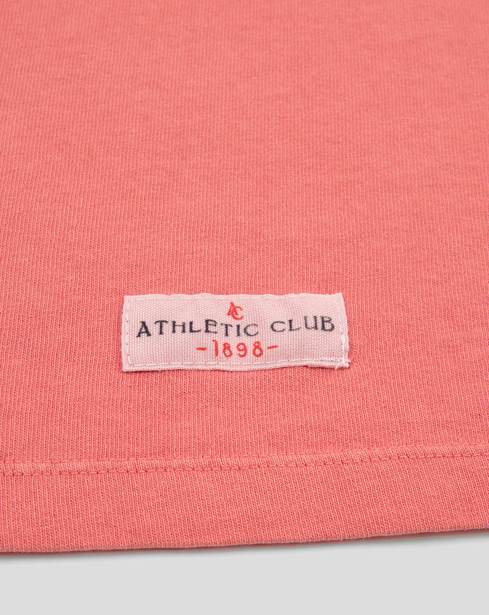 Close up of coral pink knit fabric with a small pink label reading ATHLETIC CLUB 1898 at the hem