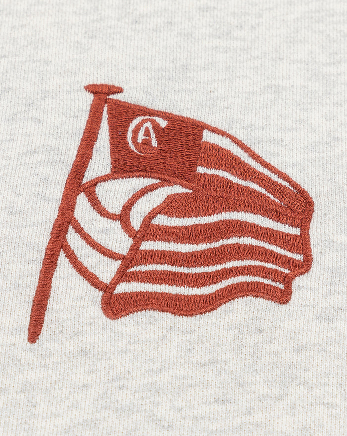 Close-up of the red flag embroidery on the chest of the heather white hoodie