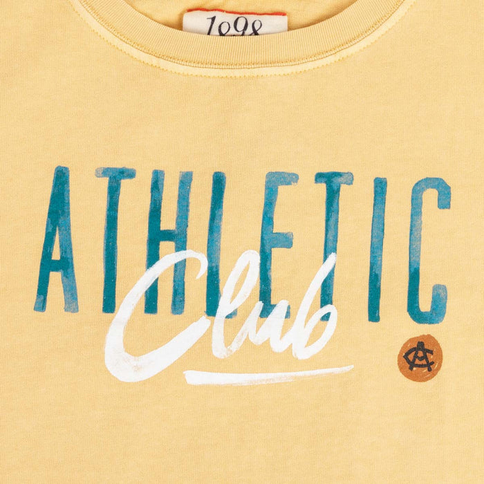 Close-up of the yellow Junior AC Collection tee showing blue Athletic letters and white Club script.