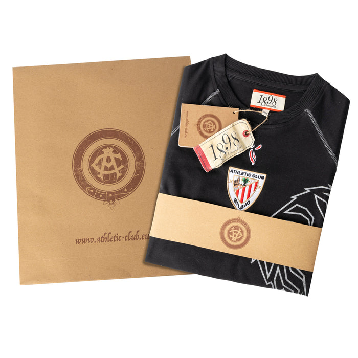 Black junior retro T shirt folded with Athletic Club Bilbao crest and 1898 tag, wrapped in kraft paper packaging.