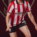 Athlete wearing red and white striped Athletic Club jersey in action with black shorts