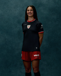 Front view of a woman wearing a black away short sleeve soccer jersey with red trim and club crest on the chest.
