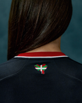 Back view of a woman in a black away short sleeve jersey with red collar and Basque flag patch on the upper back.