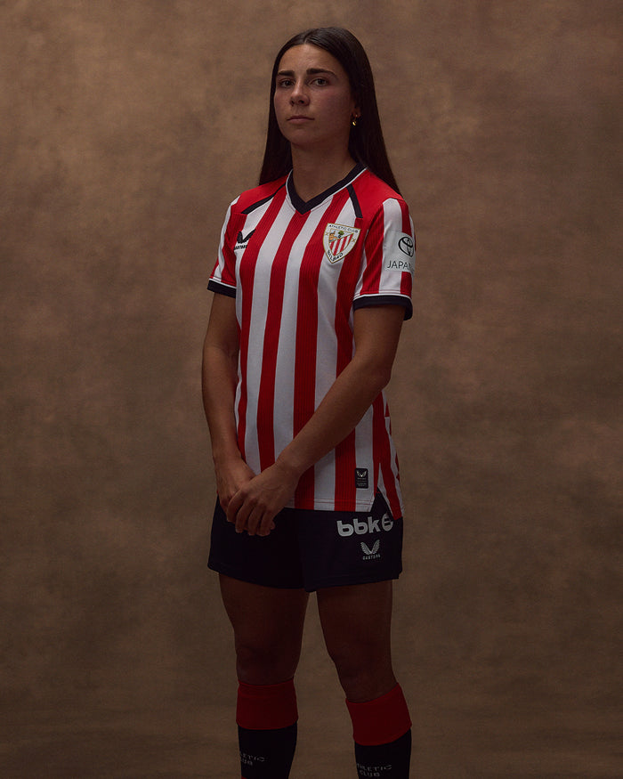 Female model wearing the 26/27 Women's Home short sleeve shirt with red and white vertical stripes and club crest.
