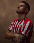 Portrait of a man wearing the red and white striped Home shirt with club crest on the chest