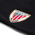 Close-up of black knit beanie showing an embroidered shield crest patch