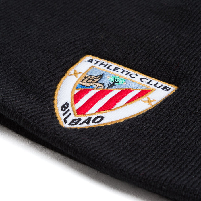 Close-up of black knit beanie showing an embroidered shield crest patch