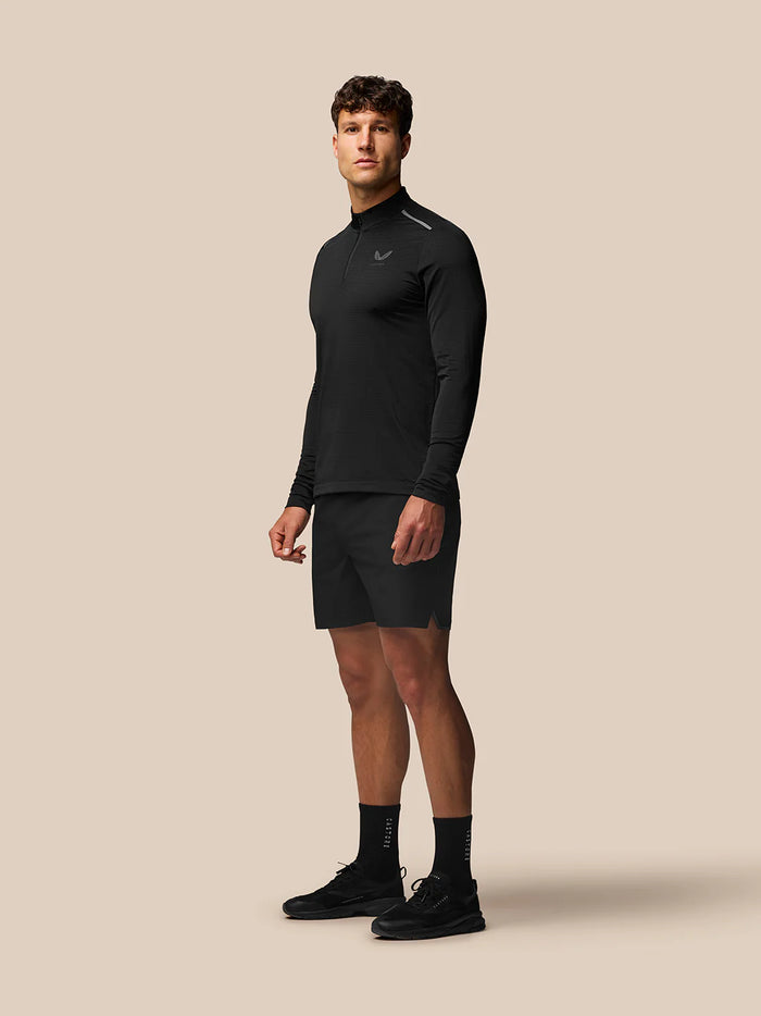 Male model wearing black Apex Training Shorts with matching long sleeve top on beige background