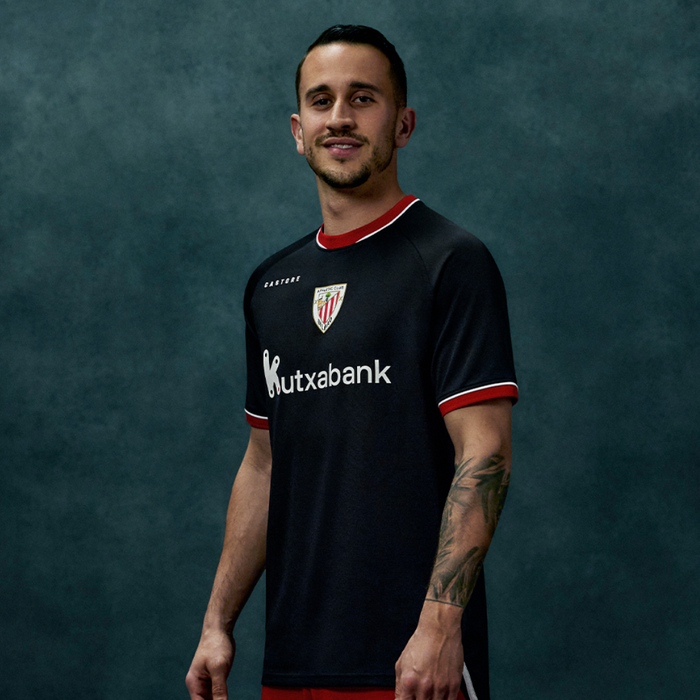 Male model wearing black away short sleeve shirt with red trim posing against teal backdrop