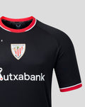 Close up of black away jersey chest area showing crest badge and red collar trim from a slightly angled perspective