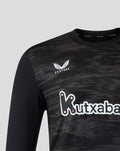 Close up of black long sleeve goalkeeper shirt showing Castore logo on chest and Kutxabank sponsor with stroke pattern.
