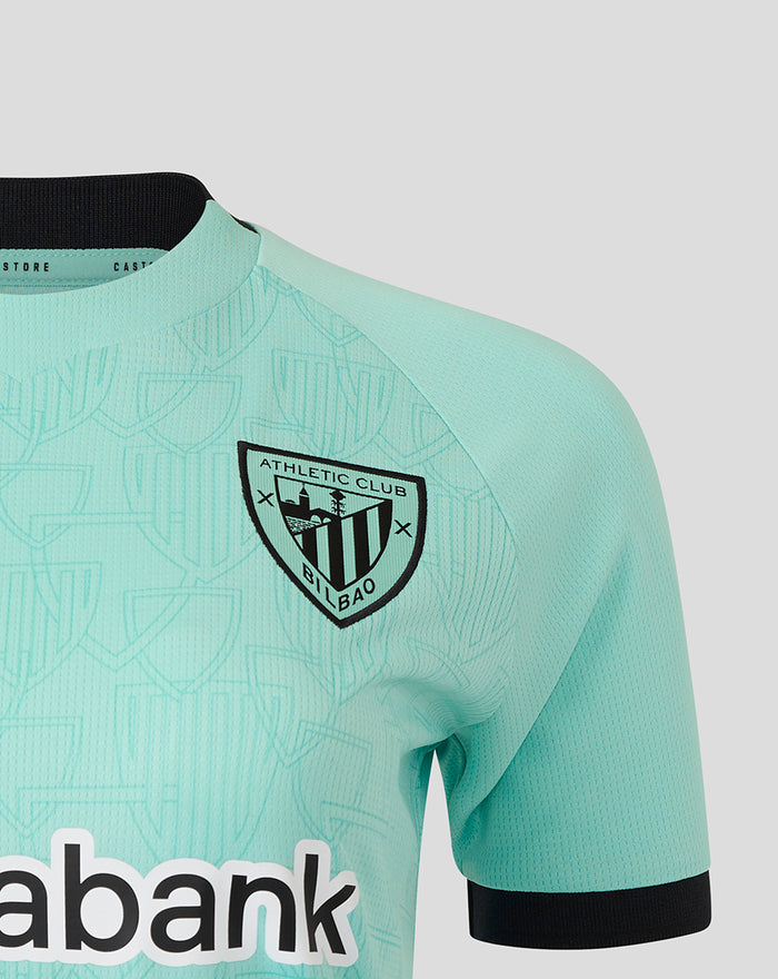 Close-up of left chest crest on turquoise Athletic Club shirt with patterned fabric and Kutxabank branding along the lower front