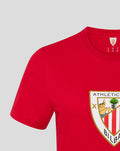 Shoulder and sleeve view of a red crest tee with the shield graphic visible on the chest