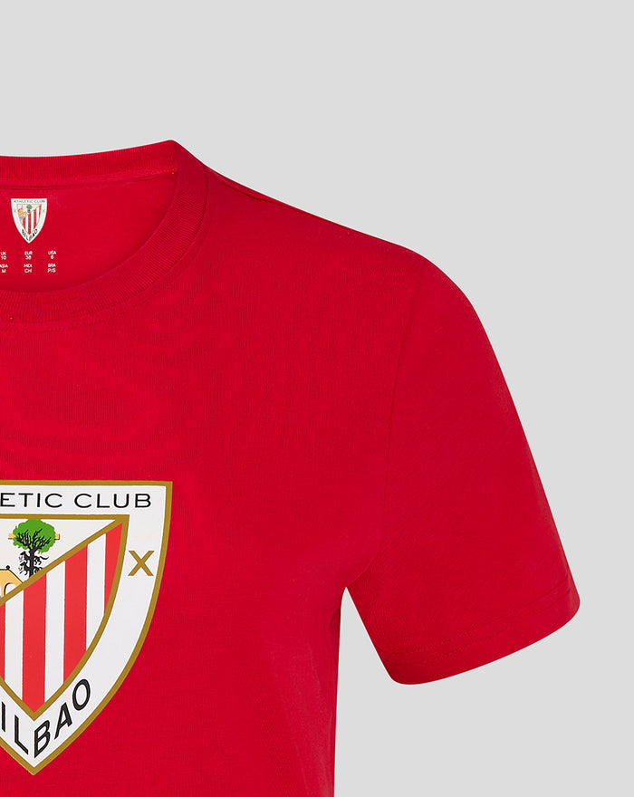 Close up of a red women's core crest tee with a partial shield emblem on the chest