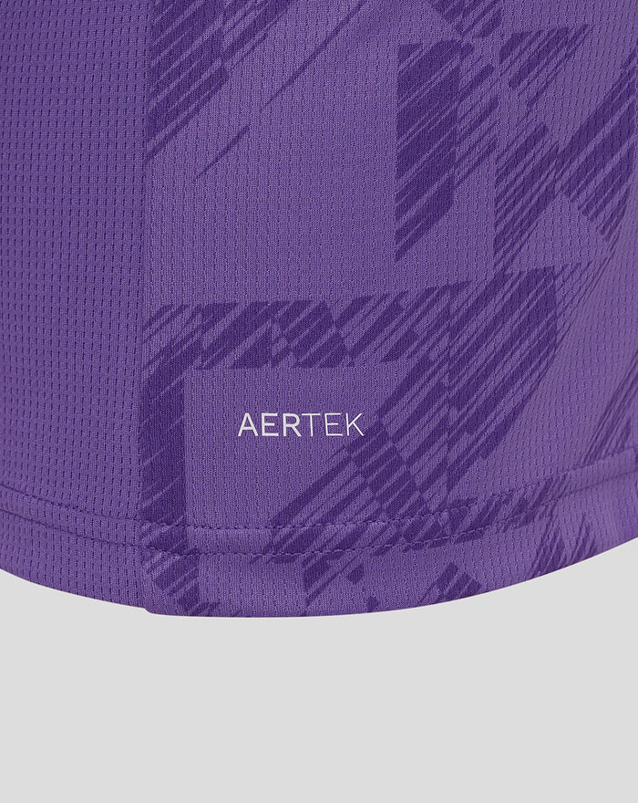 Close-up of purple fabric displaying AerTek patch and diagonal pattern near the hem of the jersey.