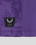 Close-up of purple fabric showing a Castore authenticity patch with wings on the lower front of the junior goalkeeper shirt.