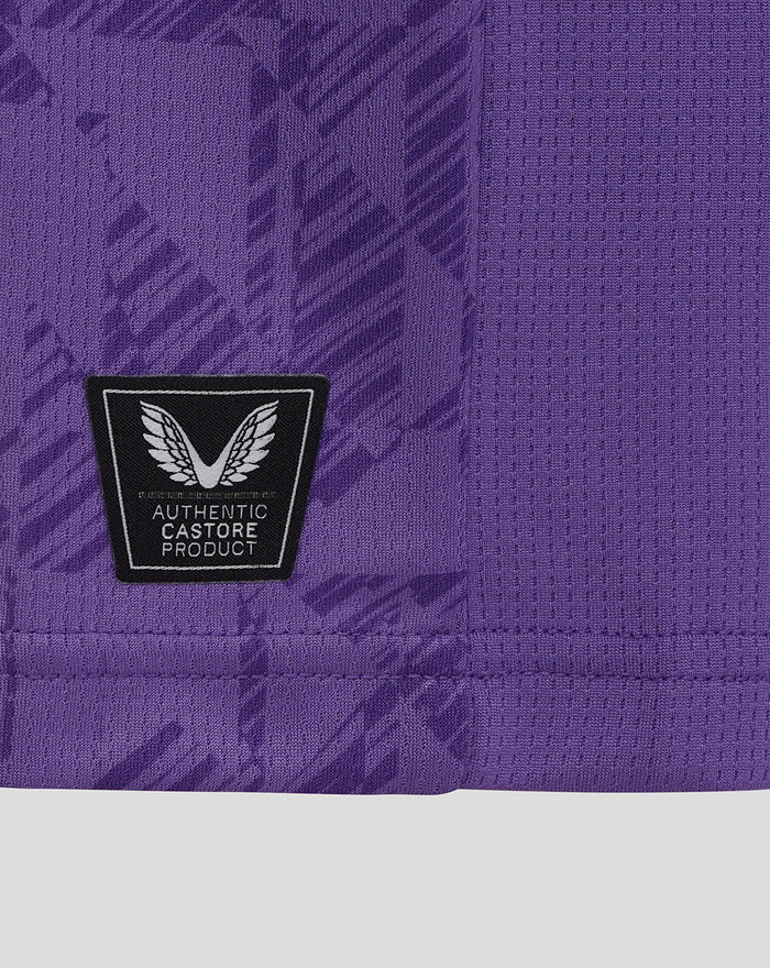 Close-up of purple fabric showing a Castore authenticity patch with wings on the lower front of the junior goalkeeper shirt.
