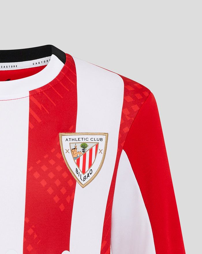 Close-up of junior home shirt chest area with red white vertical stripes and team crest.