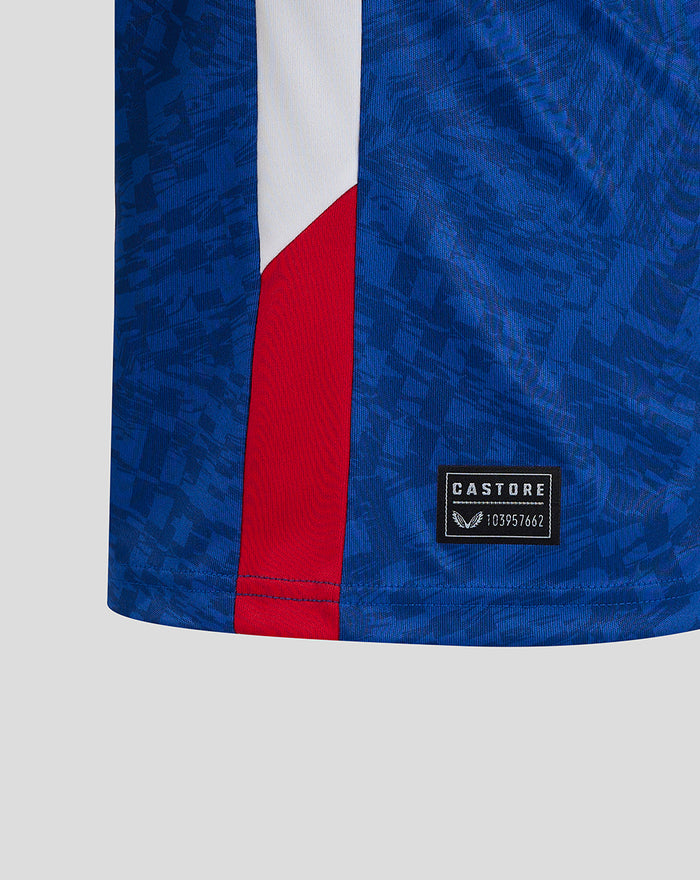 Close up of blue away shirt fabric with a white and red panel and Castore label at the hem