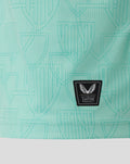 Close-up of mint turquoise athletic shirt fabric with crest pattern and Castore Authentic patch near the hem.
