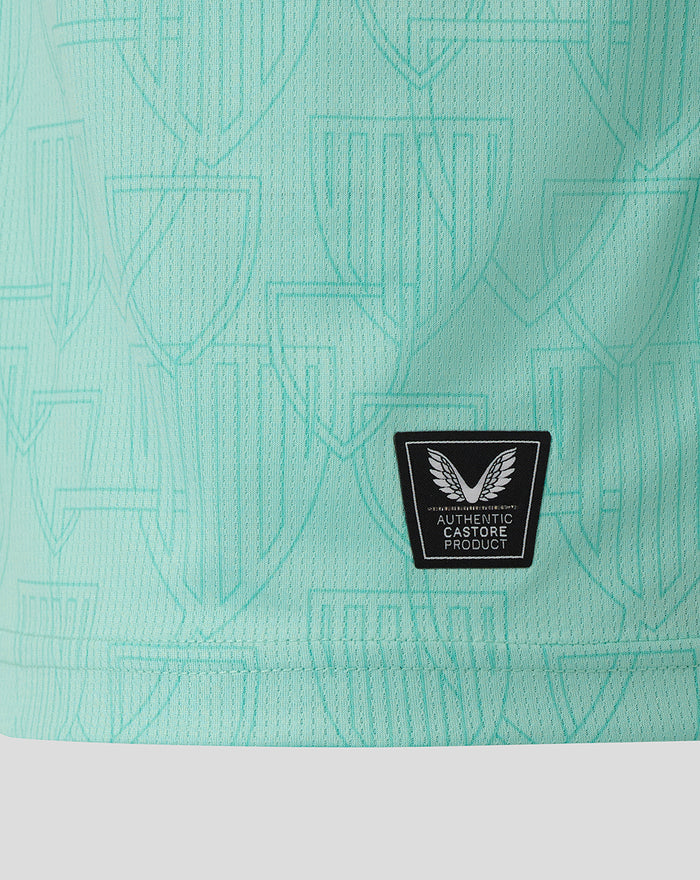 Close-up of mint turquoise athletic shirt fabric with crest pattern and Castore Authentic patch near the hem.