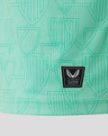 Close up of mint green athletic shirt fabric with a repeating shield crest pattern and a small black Castore authentic badge.