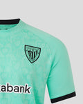 Athletic Club Bilbao crest on mint green jersey with black sleeve cuff and repeating pattern background.