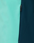 Close-up of Aruba Blue packable hooded shower jacket showing turquoise left panel and dark navy right panel with a zipper