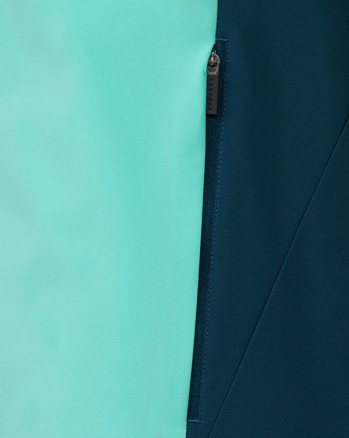Close-up of Aruba Blue packable hooded shower jacket showing turquoise left panel and dark navy right panel with a zipper