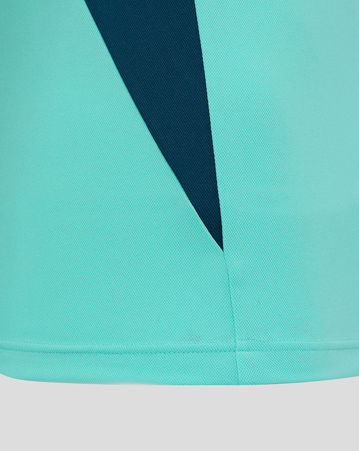 Close-up of teal polo fabric showing a dark navy diagonal panel detail.