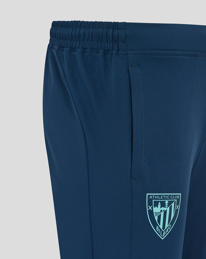 Close-up of navy Athletic Club woven pants showing elastic waistband, side pocket and crest badge.