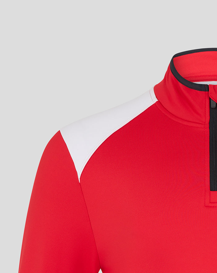 Collar and shoulder detail of the red athletic top with a black zipper and the club crest on the left chest