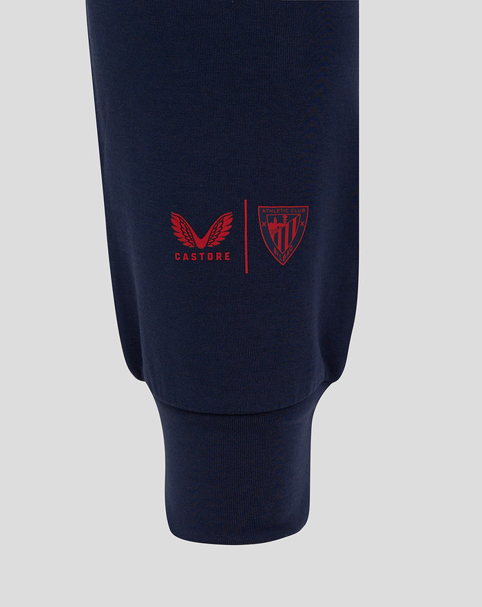 Navy men's travel pants leg with red Castore logo and Athletic Club shield near pocket area.