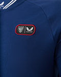 Close-up of chest patch on blue ATHLETIC CLUB COTTON POLO showing club crest and Castore logo.
