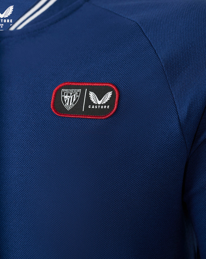 Close-up of chest patch on blue ATHLETIC CLUB COTTON POLO showing club crest and Castore logo.
