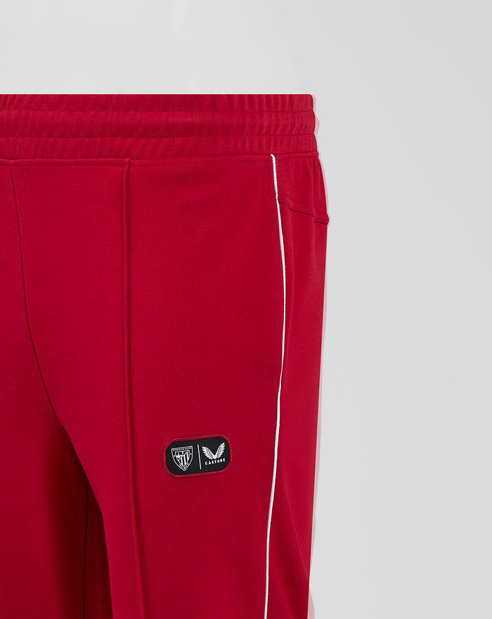 Close-up of red track pants showing white side piping and a small patch near the pocket