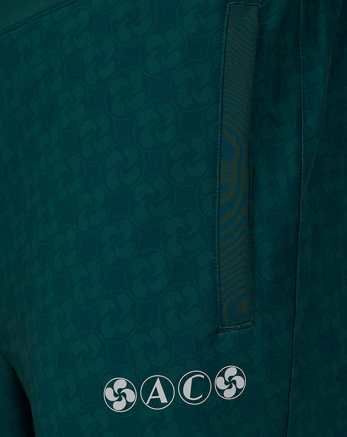 Close-up of teal patterned fabric on travel pants showing a vertical pocket opening and row of circular brand emblems near the hem
