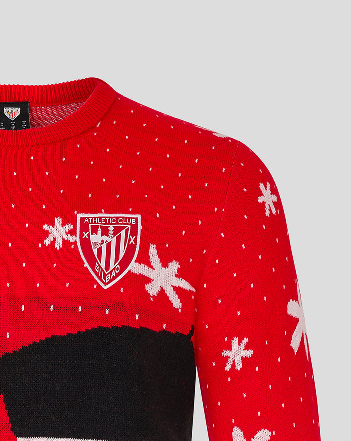 Red knit Christmas jumper with a crest badge on the chest and scattered white snowflakes