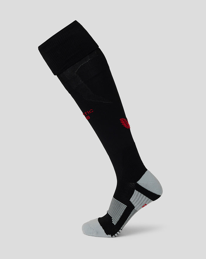 Black junior athletic soccer sock with red crest and gray heel and toe panels on a light gray background.