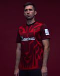 Athletic Club 4th short sleeve junior shirt worn by a model in a red and black striped design with crest and Kutxabank logo