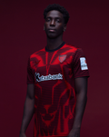 Male model wearing Athletic Club 4th short sleeve shirt with red and black pattern against a dark red studio backdrop.