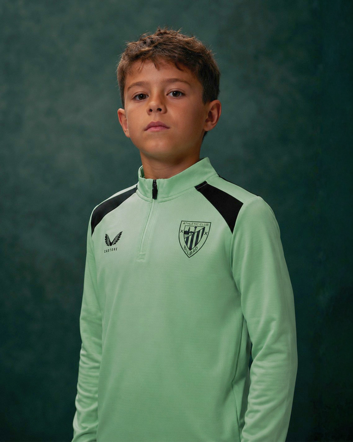 Portrait of a young boy wearing a mint green performance midlayer top with black shoulder panels and a shield crest