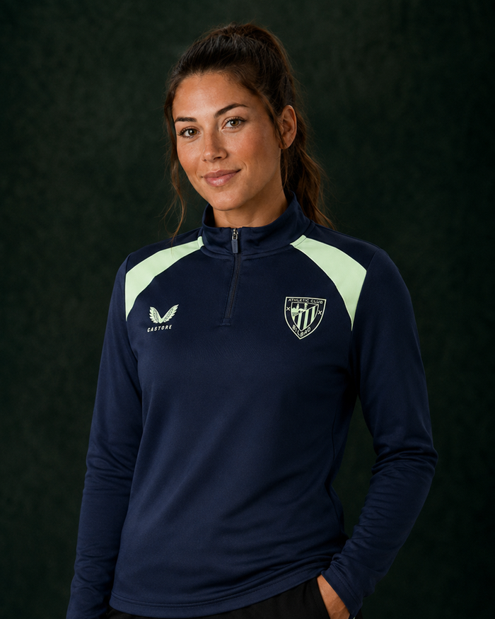Woman modeling navy performance midlayer top with pale lime shoulder panels and club crest