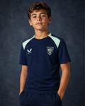 Young model wearing navy performance short sleeve tee with mint shoulder panels and a crest on the chest.