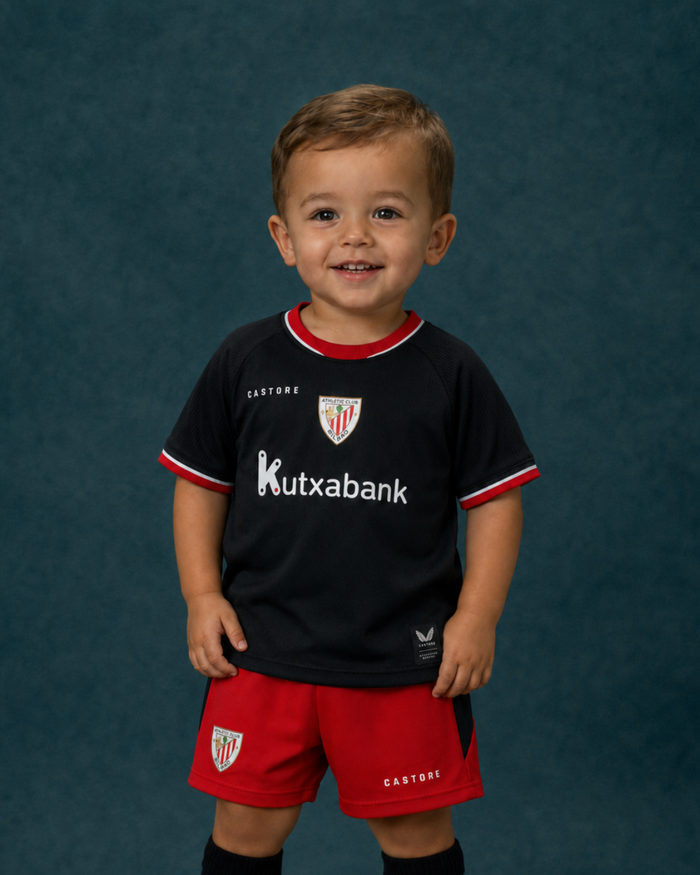 Toddler in Away Baby Kit black jersey with red shorts and Kutxabank sponsor